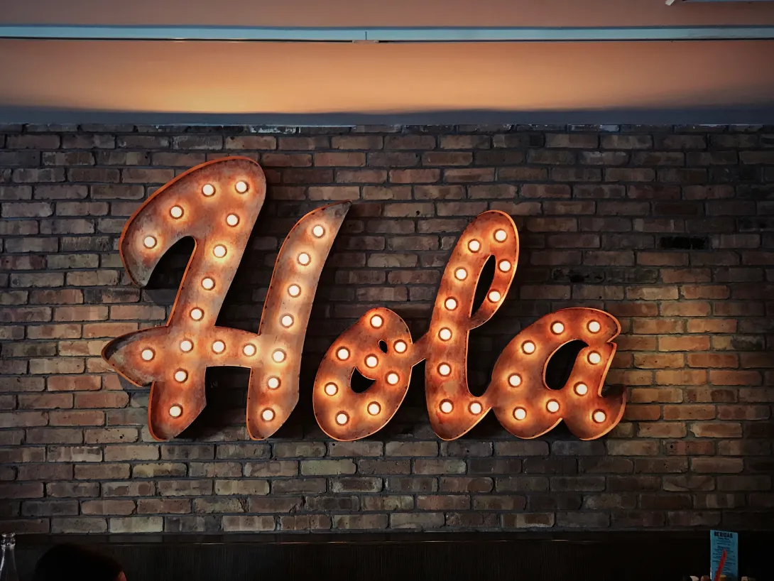 A sign made of lightbulbs spelling out the Spanish word "Hola" in an orange glow