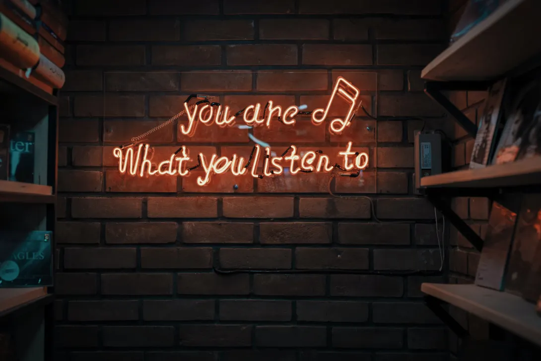A neon light sign in orange glow with the text "You are what you listen to" adorned by an eighteenth music note